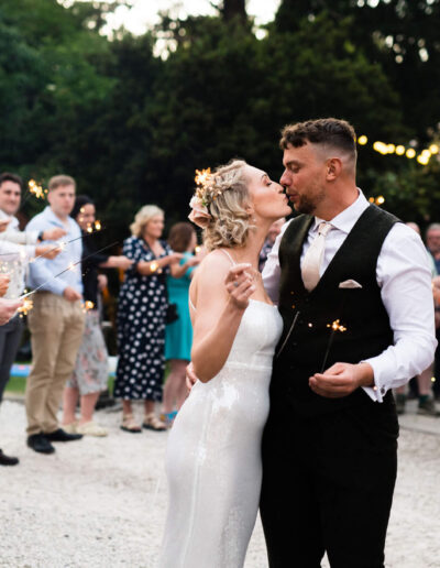 Bride and groom kissing whilst their guests hold sprinklers in the garden of St Johns House in Lichfield