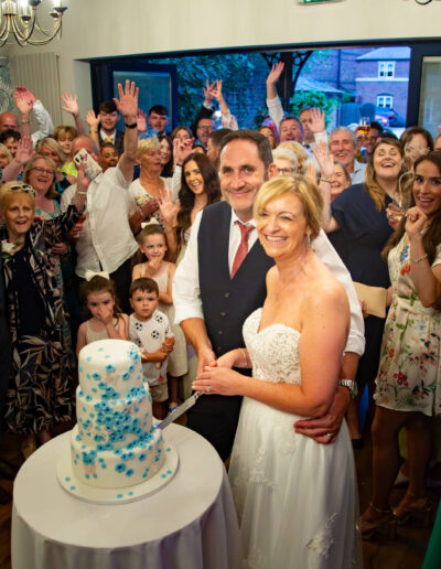 Bride and groom cutting their wedding cake with their guests behind at St Johns House in Lichfield
