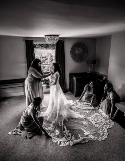 Black and white image of bridesmaids fixing a bride's dress
